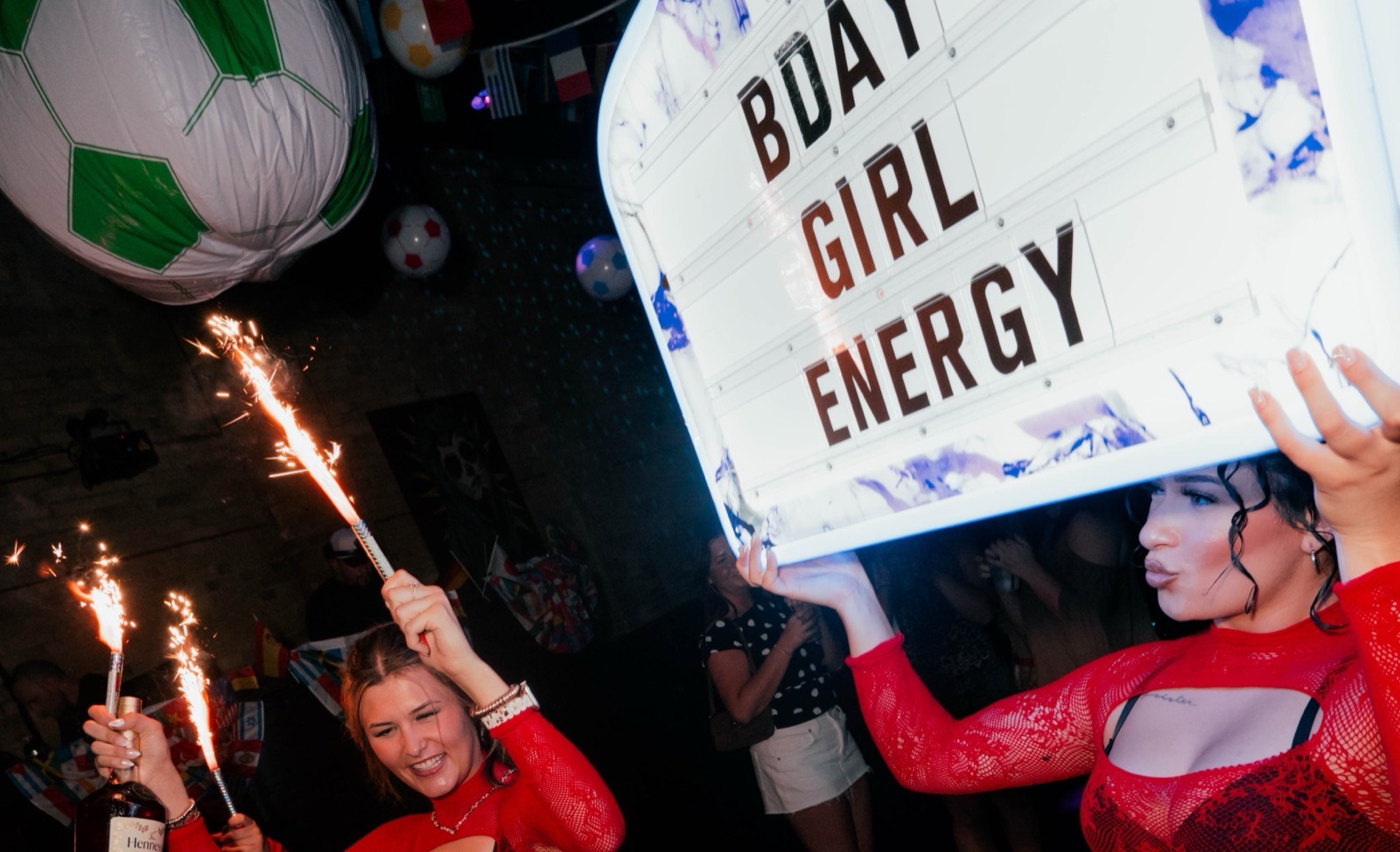 Bodega servers carrying a lit BDAY GIRL ENERGY sign and champagne sparklers through the club